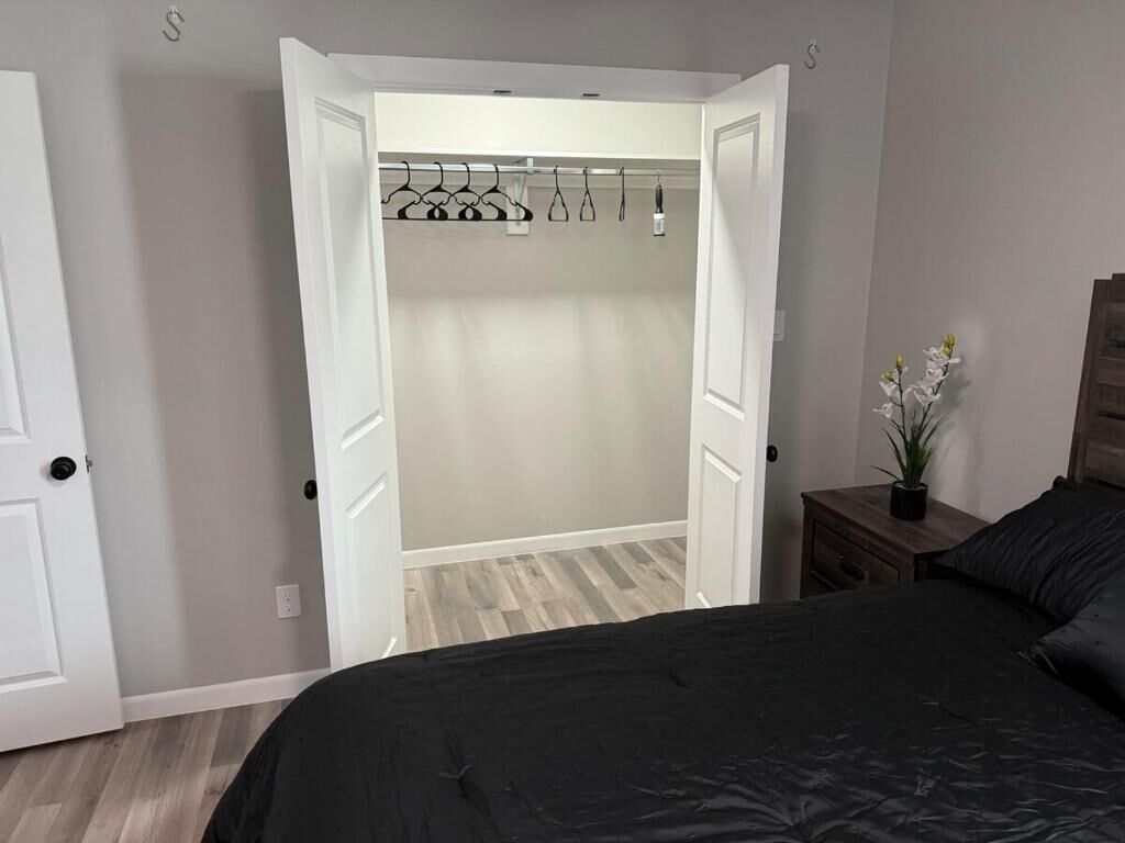 A bedroom with a bed, a nightstand with a plant, and a closet with hanging clothes.