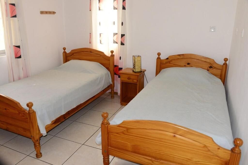 A room with two wooden beds, a bedside table with a lamp, and a window with curtains.