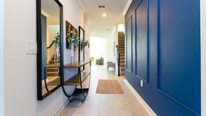 A hallway with a mirror, a console table with plants, a rug, and a staircase. - Super Luxury Modern Home, Prime Location (Kissimmee)