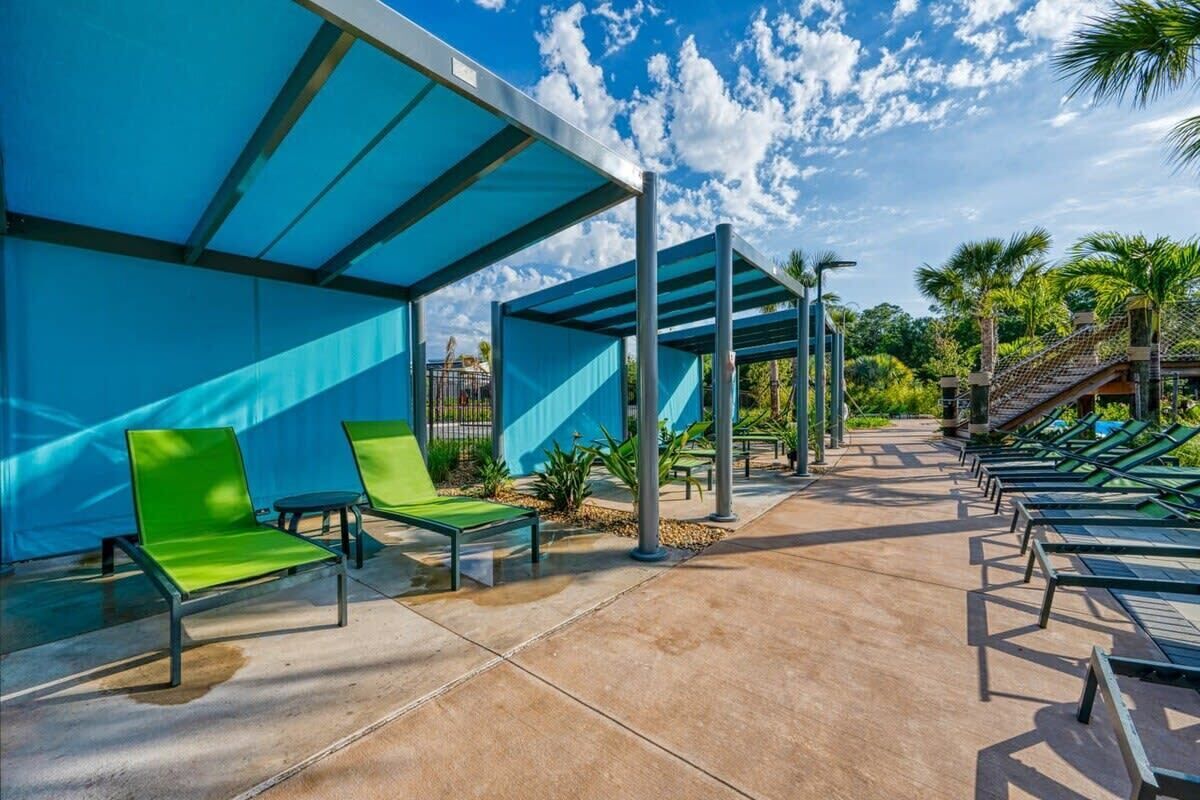 Un espace extérieur abrité, doté de fauteuils de salon verts et d’un sol en béton.