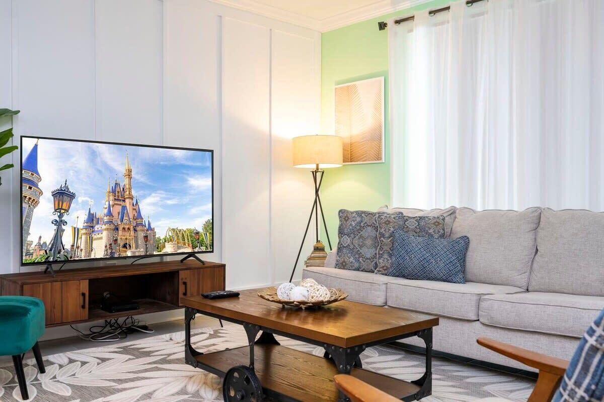 Una sala de estar con una televisión de pantalla plana, un sofá, una mesa de centro y una lámpara.