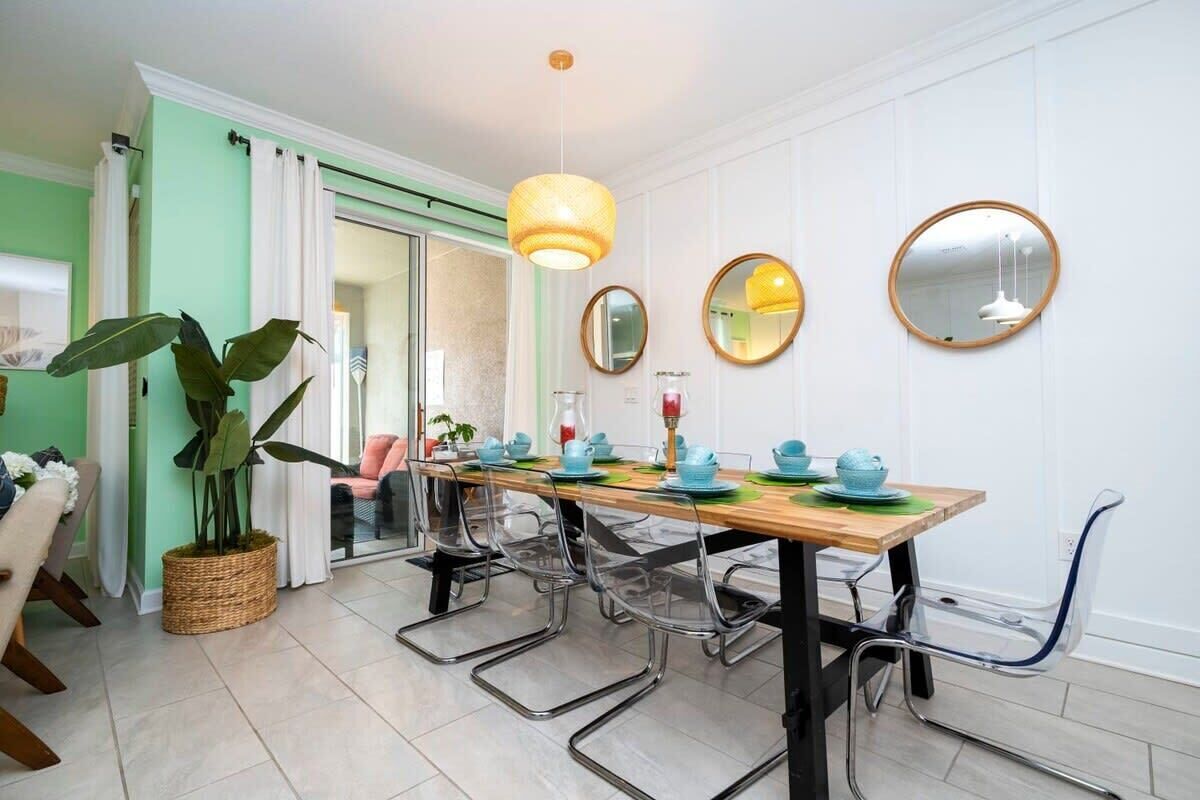 Uma sala de jantar com mesa de madeira, cadeiras transparentes e um lustre.