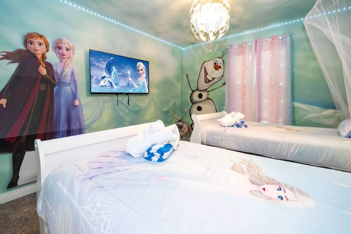 A bedroom with two beds, a wall mural, a television, and a decorative ceiling light.
