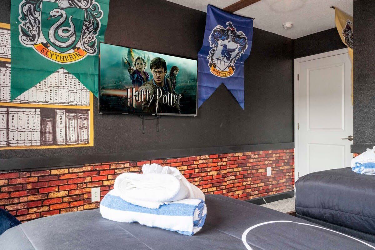 Una stanza con una TV a schermo piatto che mostra un film di Harry Potter, un letto con asciugamani piegati con cura e due striscioni che raffigurano le case di Hogwarts.