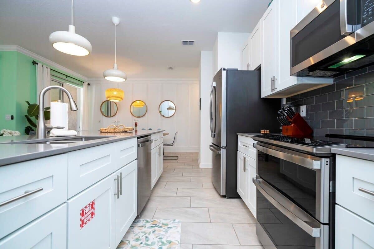 A modern kitchen with white cabinets, stainless steel appliances, and pendant lighting.