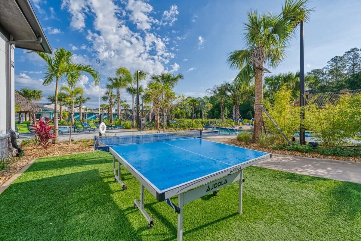 A ping pong table in a well-maintained outdoor area with palm trees and a clear sky.