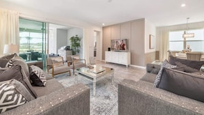 A modern living room with a glass coffee table, grey sofas, and a TV on a cabinet. - Stunning Retreat, Private Pool, Perfect Location (Kissimmee)