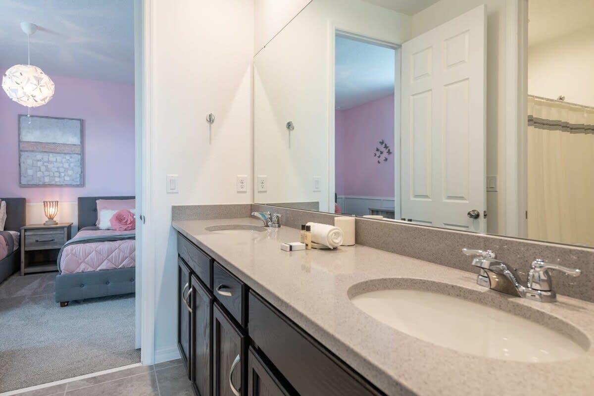 Une salle de bain moderne avec un double vasque, un grand miroir et un lit dans la pièce adjacente.