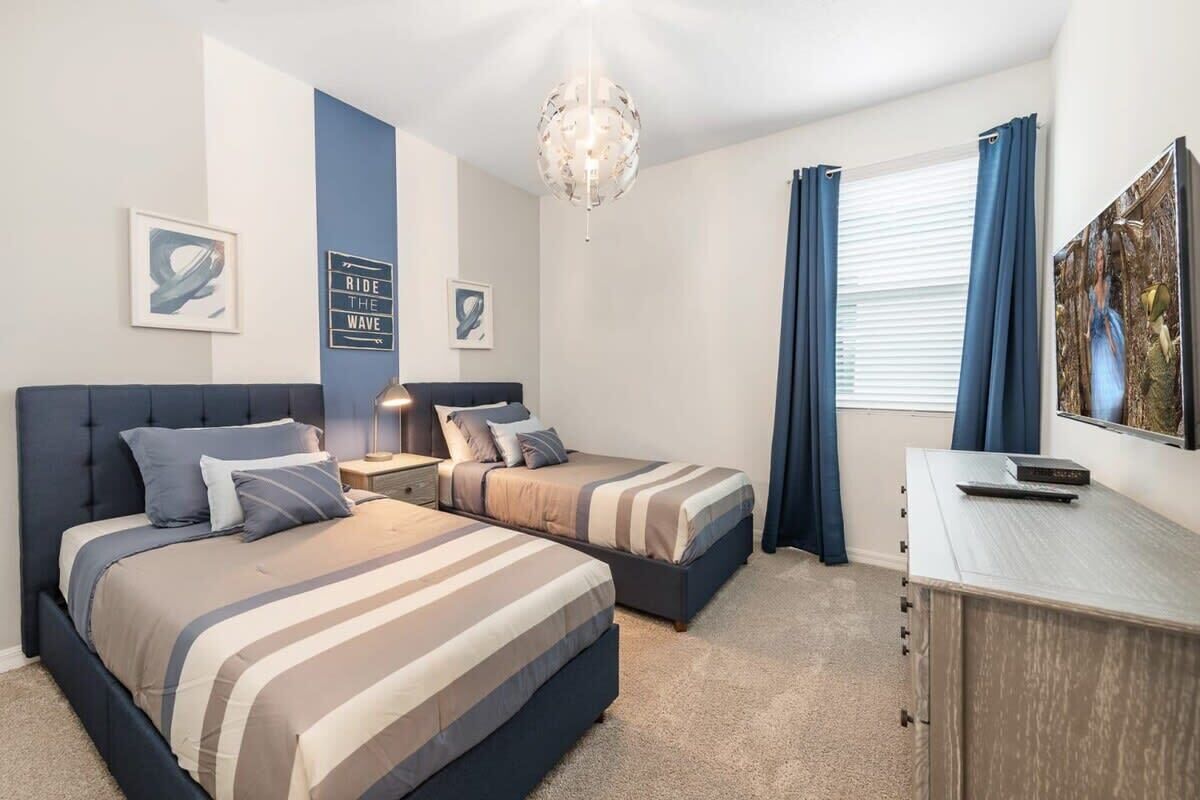 A bedroom with two beds, a desk, a chandelier, and artwork on the walls.