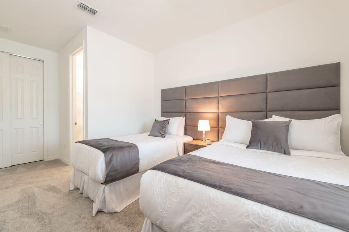 A hotel room with two beds, a headboard, bedside tables, and a door.