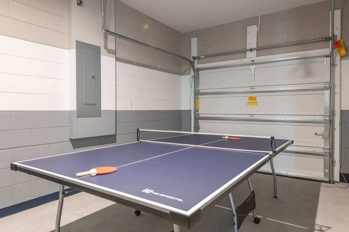 A ping pong table with a paddle in the center, set against a wall with a metal rack and a door.