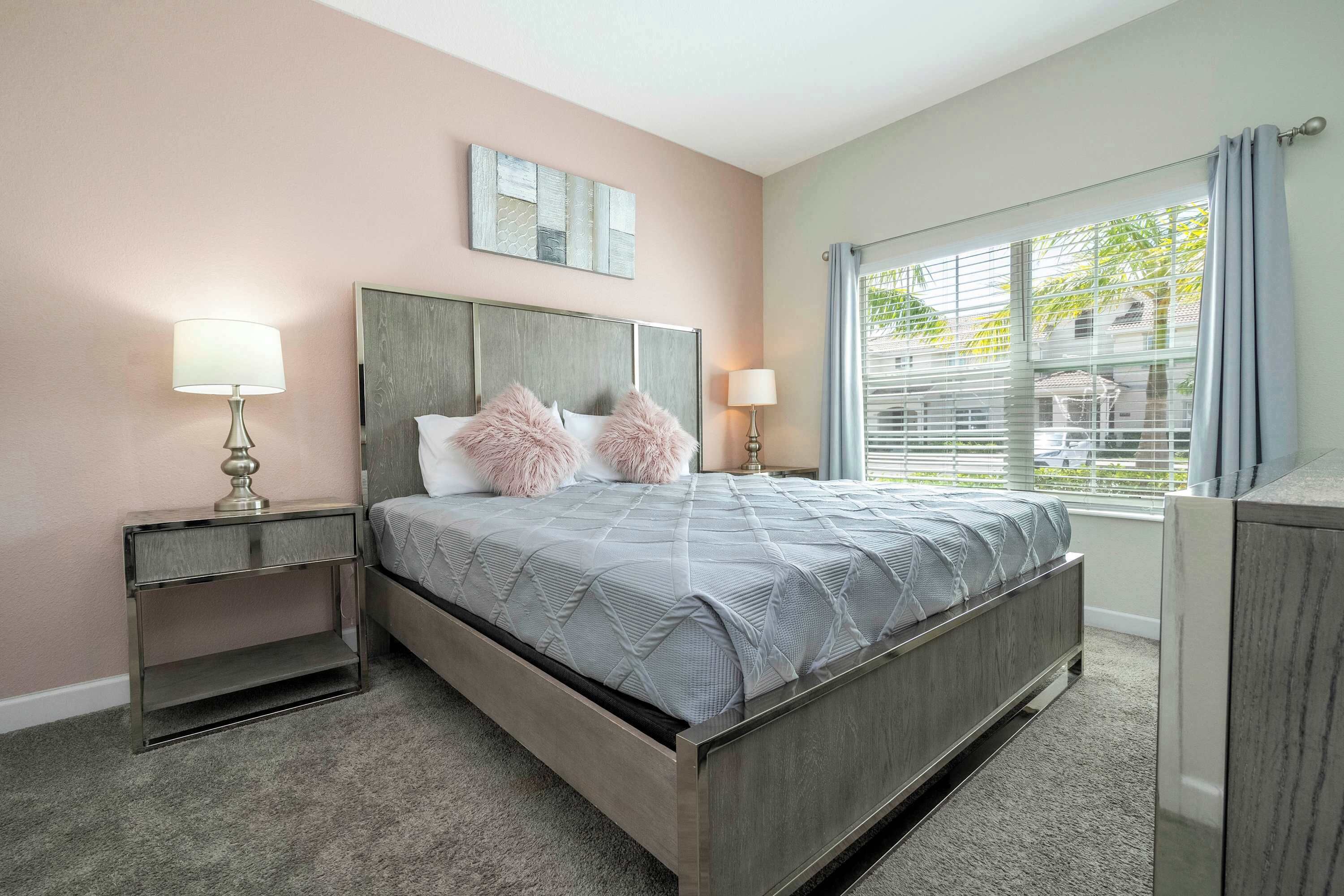 A bedroom with a bed, two bedside tables, a window with curtains, and a wall-mounted mirror.