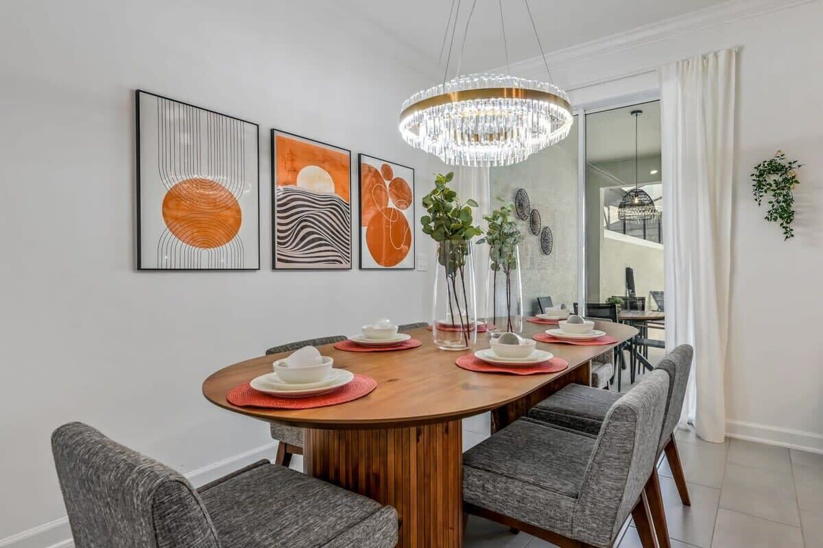 Un comedor con una mesa de madera, sillas tapizadas de color gris y una lámpara de araña.