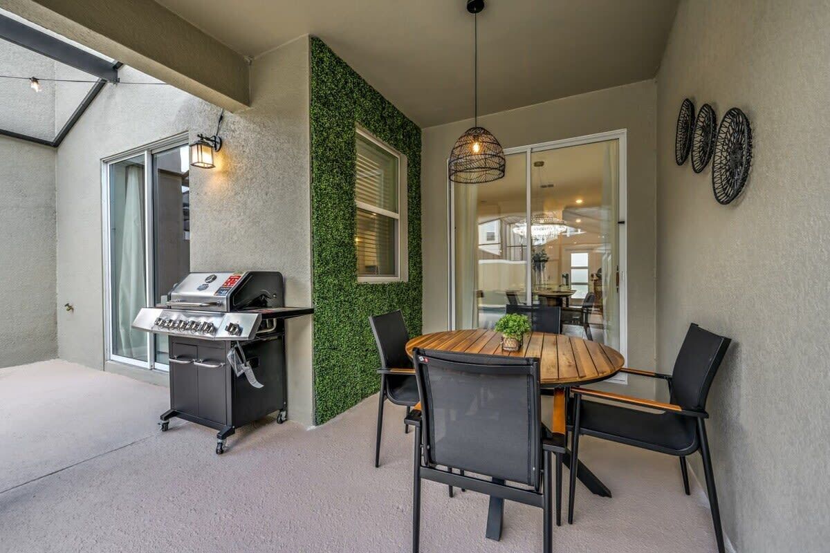 Een terras met een barbecue, een eettafel met stoelen en een glazen deur die leidt naar een binnenruimte.