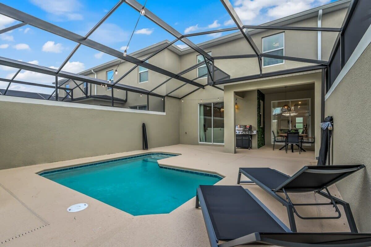 A rooftop pool with clear blue water, surrounded by lounge chairs, and a glass-enclosed patio area.