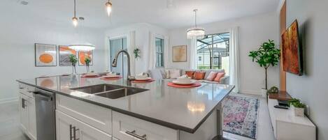 A modern kitchen with a central island, stainless steel appliances, pendant lighting, and a view to the outside.