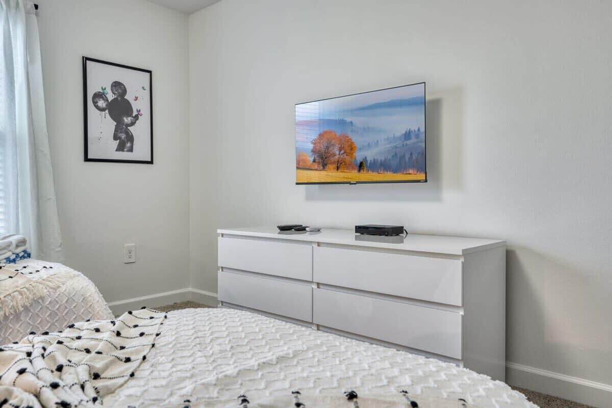Un dormitorio con una cama, un aparador blanco, un cuadro enmarcado y un televisor en la pared.