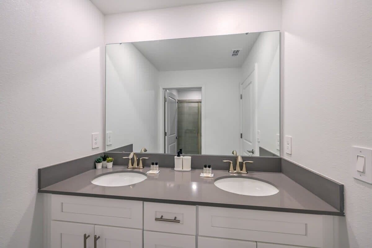 A bathroom with two sinks, a large mirror, and a door leading to another room.