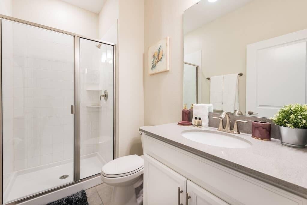 A bathroom with a glass shower enclosure, a toilet, a sink with a mirror, and a potted plant.
