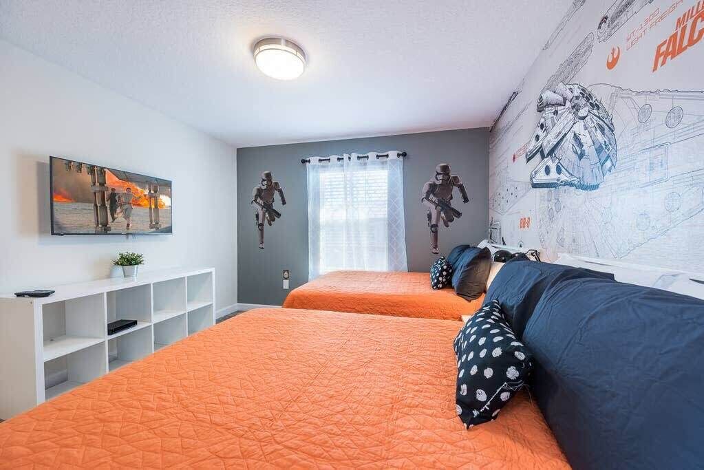 Quarto com duas camas, televisão, prateleira e um mural na parede.