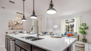 Cocina moderna con una isla grande, iluminación colgante y vistas al área de estar.