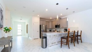 A modern kitchen with a marble island, stainless steel appliances, and wooden chairs. - Super Nice and Spacious 9bdr Home (Davenport)