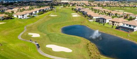 A golf course with bunkers, a pond, and residential buildings in the background.