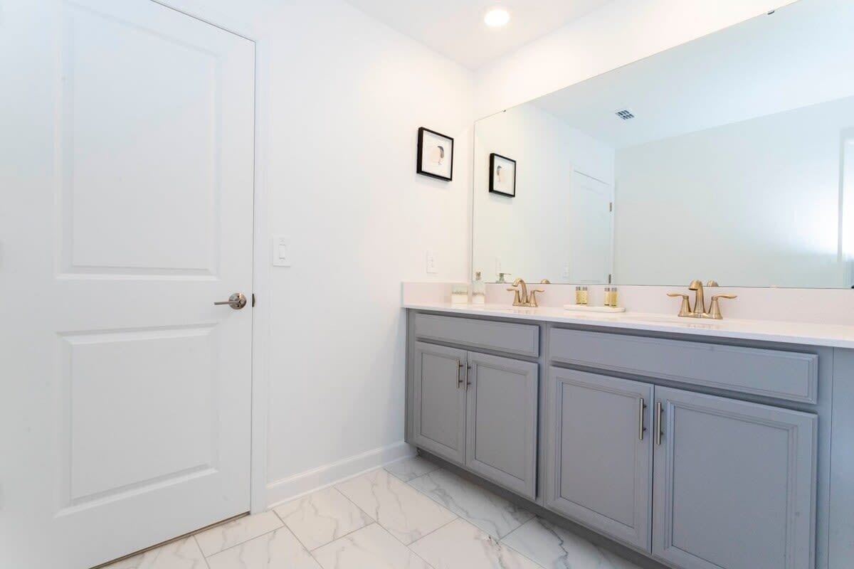 A bathroom with a white door, a large mirror, a vanity with a white countertop, and grey cabinets.
