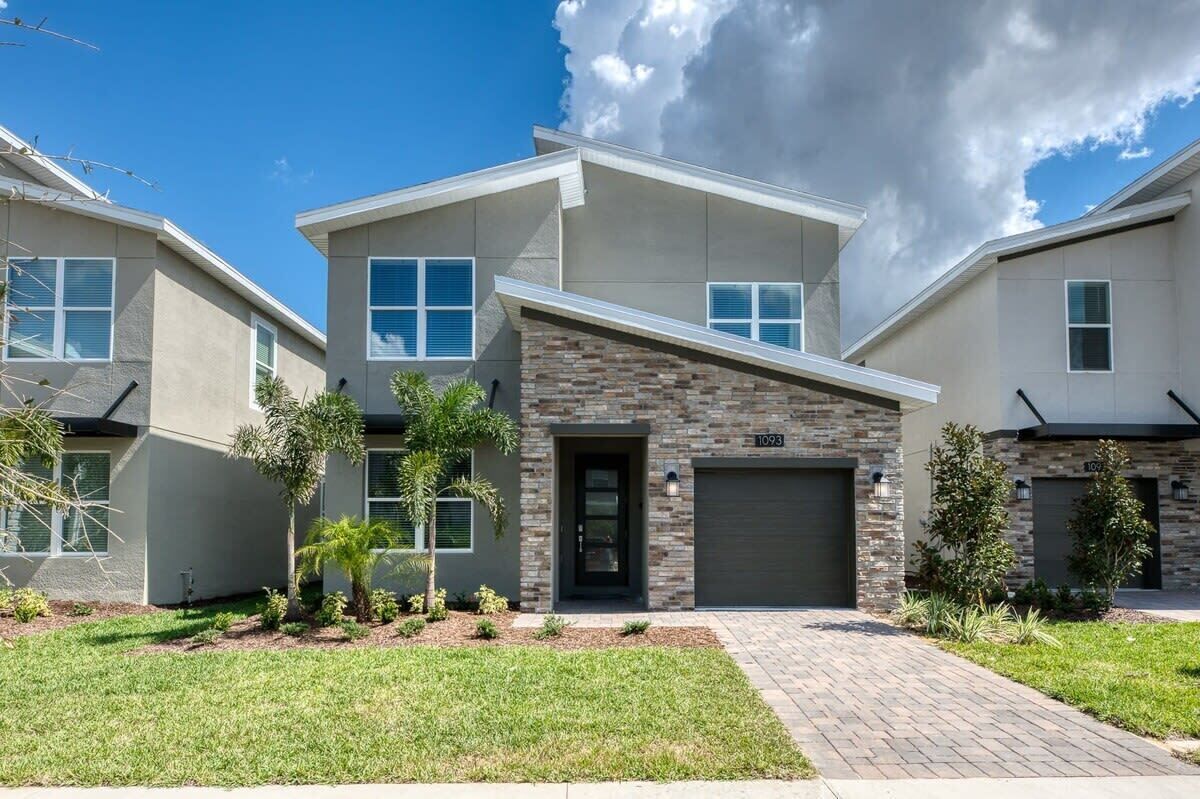 A modern two-story house with a stone facade, a garage, and a well-maintained lawn.