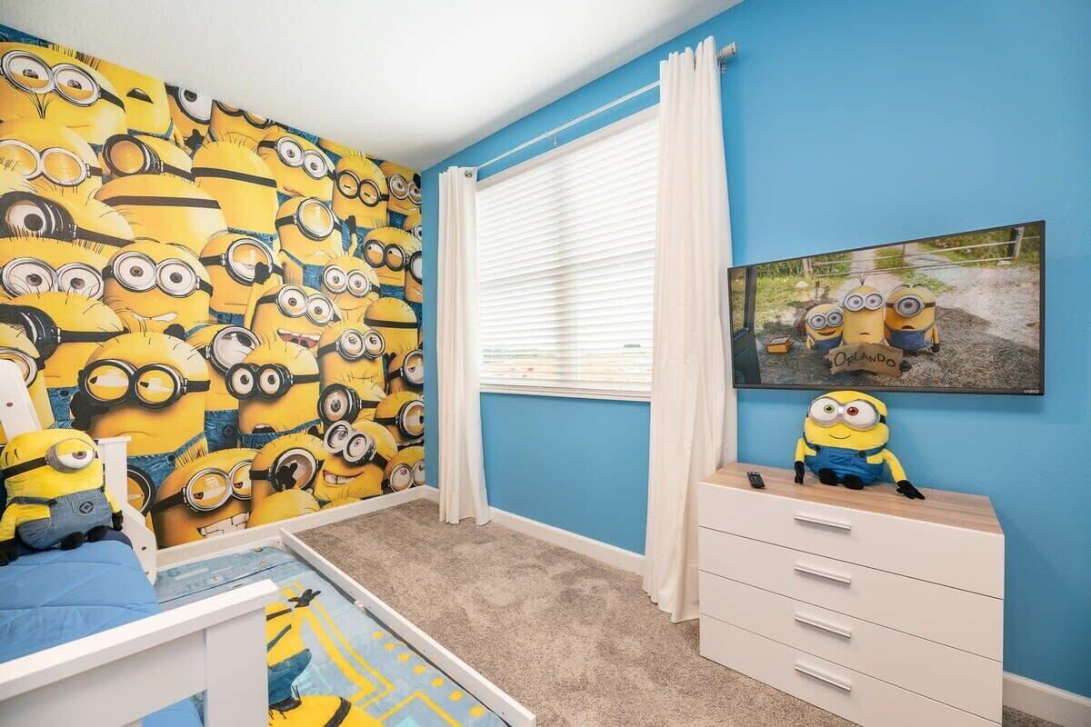 A child's room with a minion-themed wallpaper, a bed, a dresser, and a window with curtains.