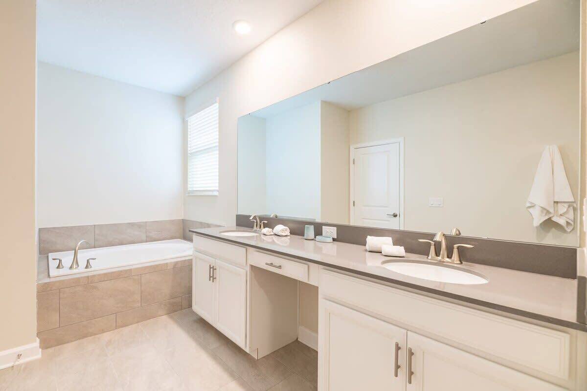 A modern bathroom with a bathtub, two sinks, a large mirror, and a door.