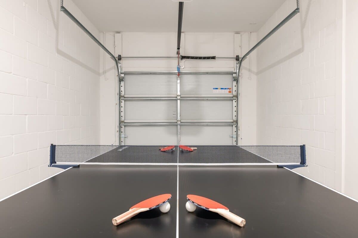 Un tavolo da ping pong con due racchette, una rete e un mobiletto portaoggetti in metallo sullo sfondo.