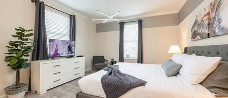 A bedroom with a bed, a TV, a dresser, a plant, and a ceiling light fixture.
