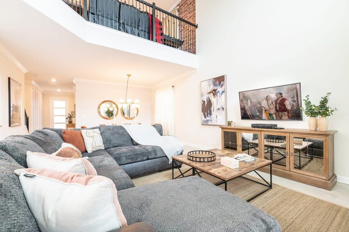Een ruime woonkamer met een hoekbank, een salontafel, een televisie op een houten kast, en een balkon met wasgoed.