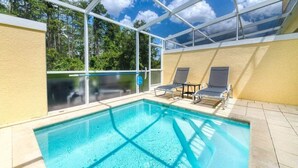 Piscina com duas espreguiçadeiras, rodeada por paredes de vidro e vista para árvores.
