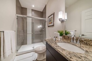 Une salle de bain moderne dotée d’une douche à parois de verre, de toilettes, d’un lavabo avec un plan de travail en granit et d’un miroir fixé au mur.