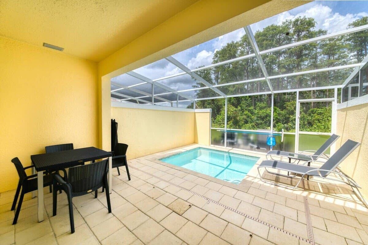 Zona de piscina con cerramiento de vidrio, una mesa con sillas y un área de descanso junto a la piscina.