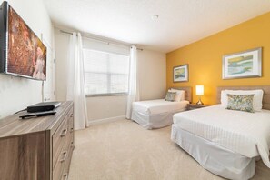 Une chambre d’hôtel avec deux lits, un bureau doté d’un téléviseur à écran plat, une commode, une fenêtre avec des rideaux et deux tableaux accrochés au mur.