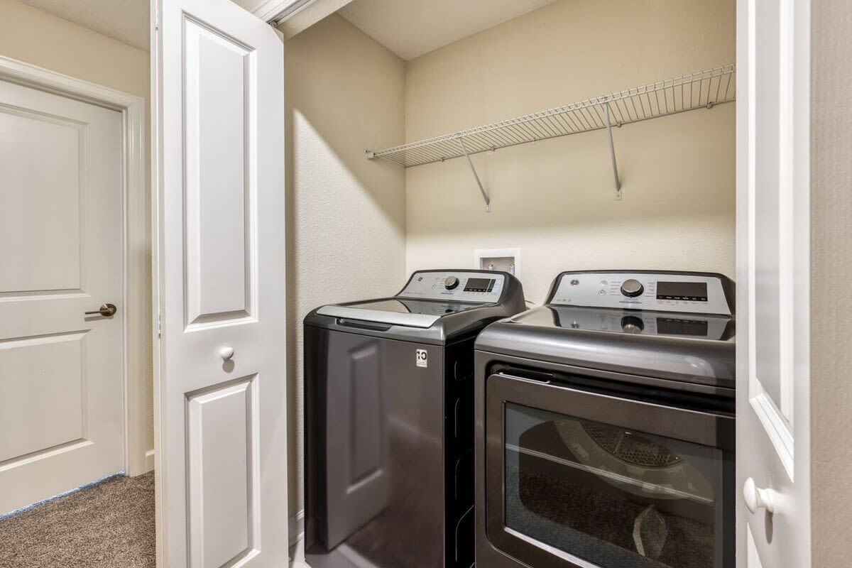 A laundry room with two stacked washers and dryers, a metal drying rack, and a white door.