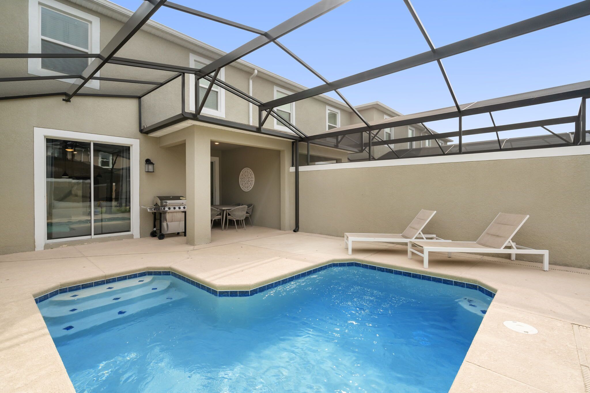 Ein Pool mit Liegestühlen, einem Grill und einer überdachten Terrasse.