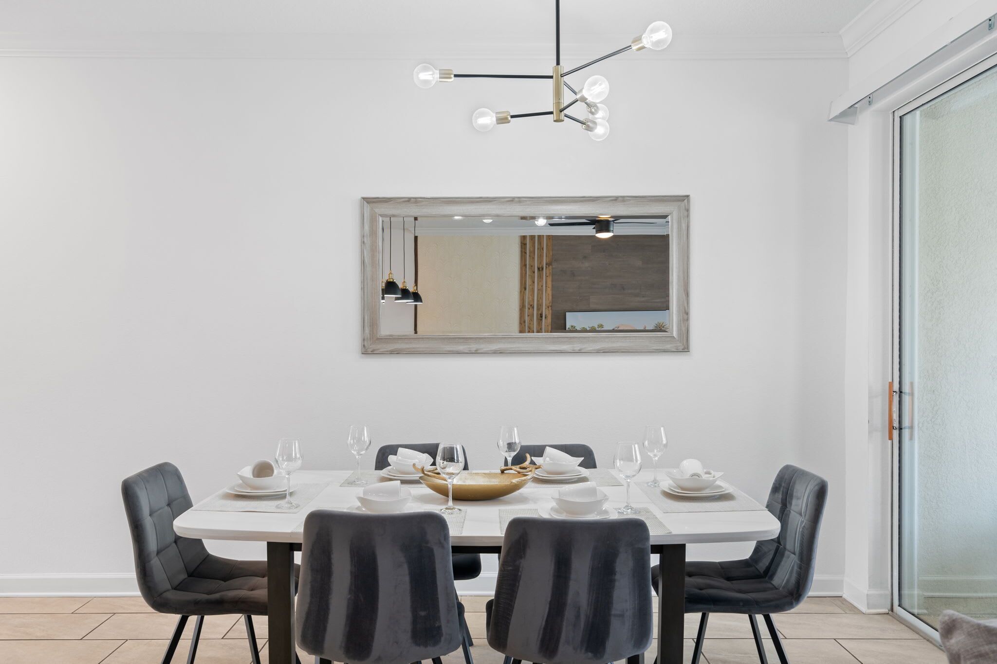 Ein Essbereich mit weißem Tisch, schwarzen Stühlen, einer modernen Kronleuchter und einem großen Spiegel an der Wand.