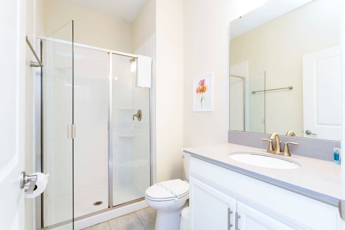 Ein Badezimmer mit Duschkabine aus Glas, einer weißen Toilette, einem Waschbecken mit Spiegel und einem gerahmten Bild an der Wand.