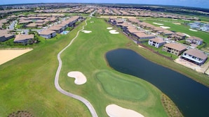 Vue aérienne d’un terrain de golf avec des bunkers de sable, un obstacle d’eau et des immeubles résidentiels.