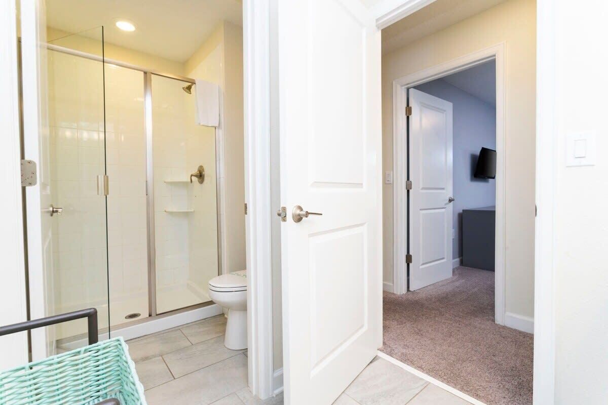 Un baño con cabina de ducha de vidrio, inodoro y puerta blanca que da a un pasillo.