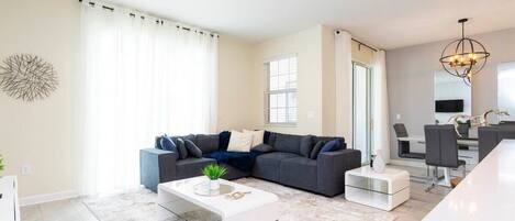 A modern living room with a sectional sofa, a coffee table, and a dining area with chairs and a table.