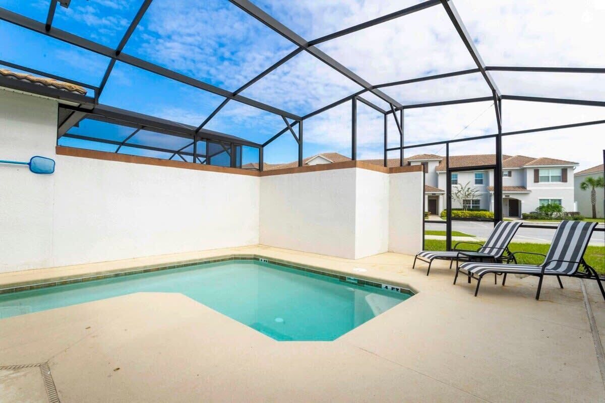 Una piscina con cerramiento de vidrio, rodeada de un patio con sillones de descanso.