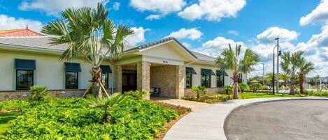 A modern building with a curved driveway, palm trees, and a clear blue sky.