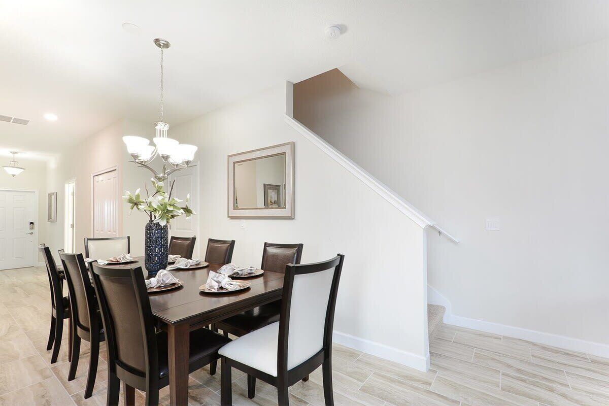 A dining area with a dark wooden table, six chairs, a vase with flowers, and a chandelier.