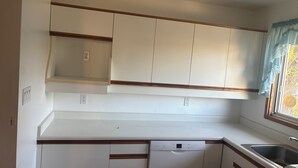 A kitchen with white cabinets, a Bosch dishwasher, and a window with a curtain. - Monthly Rentals (Edmonton)