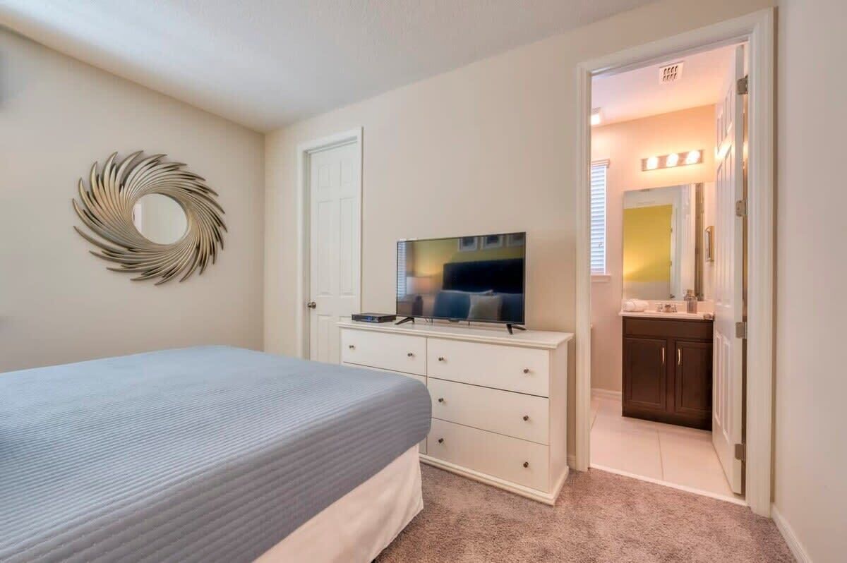 A bedroom with a bed, a dresser, a TV, and a mirror.